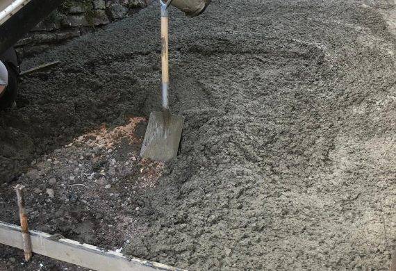 A concrete driveway being laid with a shovel in it.